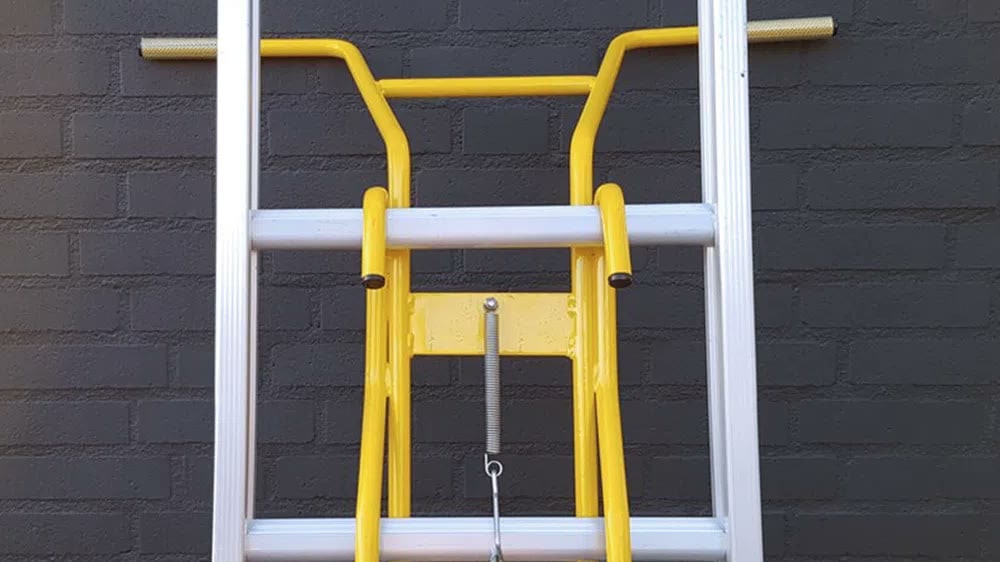 Gele wandafhouder bovenaan een ladder tegen een bakstenen muur